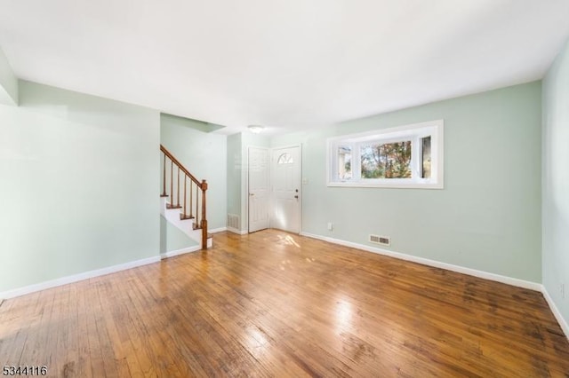 unfurnished living room with visible vents, stairs, baseboards, and hardwood / wood-style floors