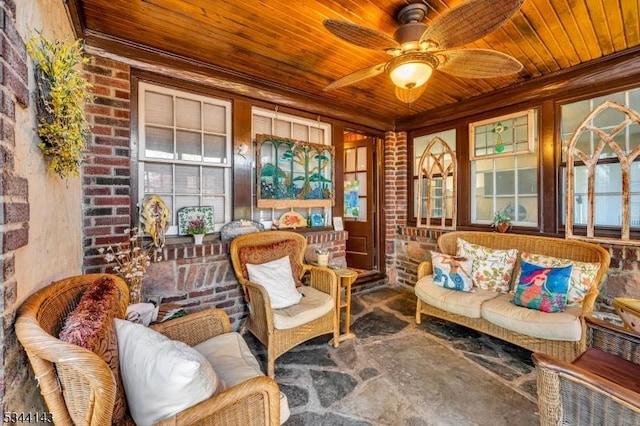 sitting room featuring a ceiling fan, brick wall, and wooden ceiling