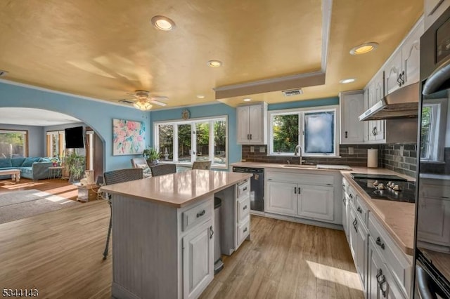 kitchen featuring arched walkways, a ceiling fan, backsplash, under cabinet range hood, and dishwashing machine