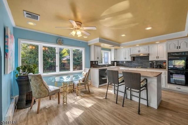 kitchen with white cabinetry, backsplash, under cabinet range hood, visible vents, and black appliances