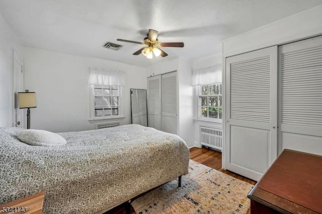 bedroom with visible vents, radiator, multiple closets, wood finished floors, and ceiling fan