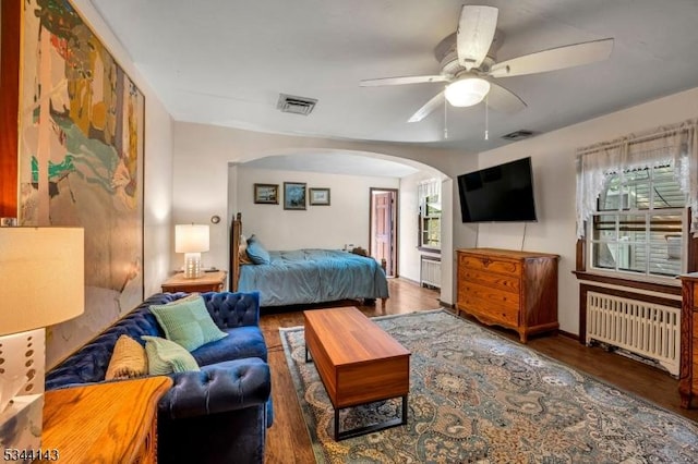 bedroom featuring ceiling fan, arched walkways, radiator, wood finished floors, and visible vents