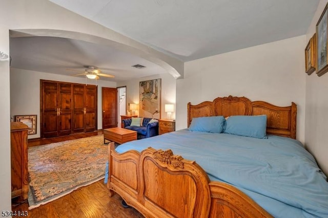 bedroom with arched walkways, a ceiling fan, visible vents, and wood finished floors
