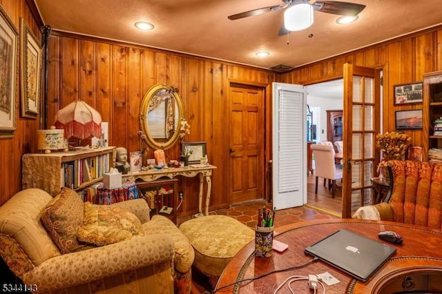 living area featuring ceiling fan and wood walls