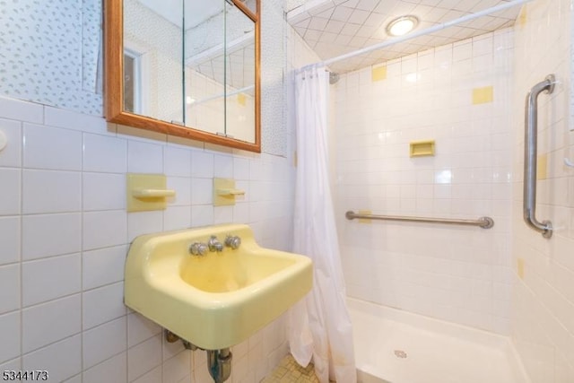 full bathroom with tile walls, a shower stall, wallpapered walls, and a sink