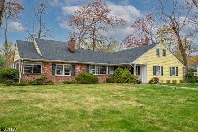 view of front facade with brick siding, a front yard, a shingled roof, and a chimney