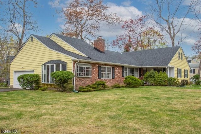 view of front of house with a chimney, brick siding, a garage, and a front yard