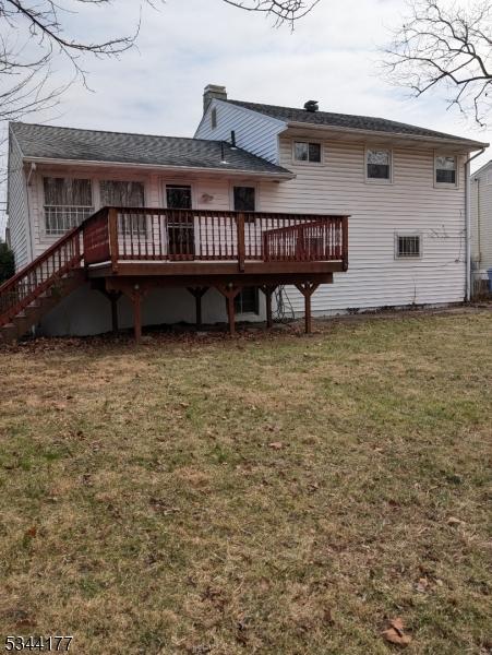 rear view of house with a deck, a lawn, and a chimney