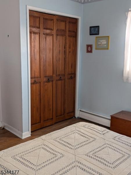 bedroom featuring a baseboard heating unit, baseboards, a closet, and dark wood-style flooring