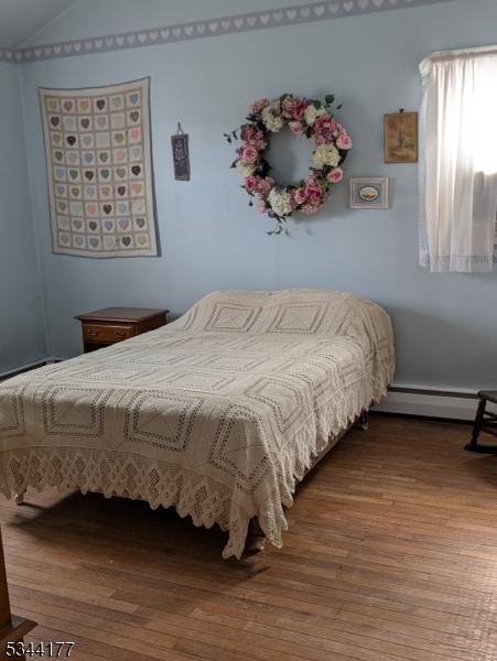 bedroom with a baseboard radiator, hardwood / wood-style floors, and vaulted ceiling