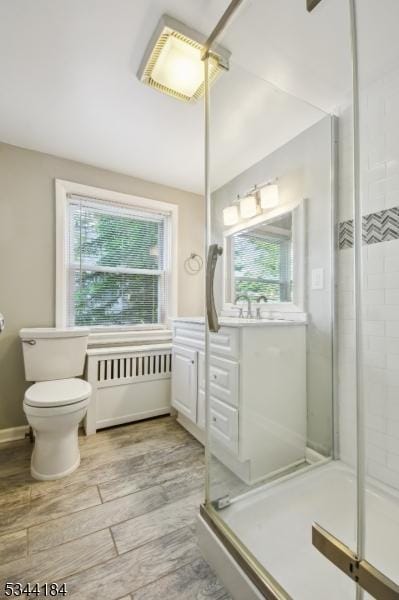 bathroom featuring radiator heating unit, a shower stall, toilet, wood finished floors, and vanity