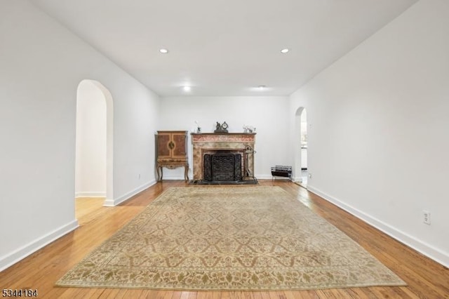 unfurnished living room featuring arched walkways, wood finished floors, a fireplace, baseboards, and recessed lighting