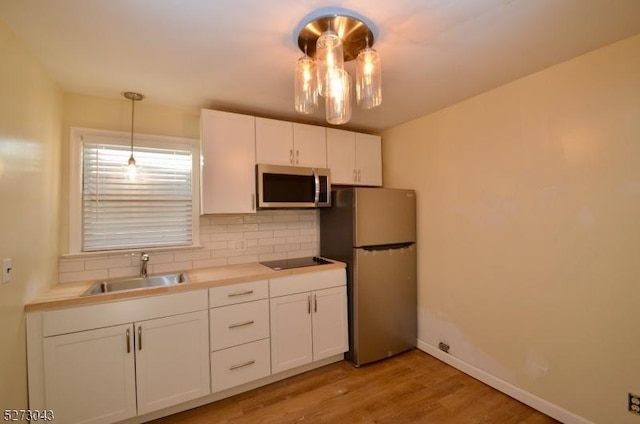 kitchen with backsplash, stainless steel appliances, light wood-style floors, white cabinetry, and a sink