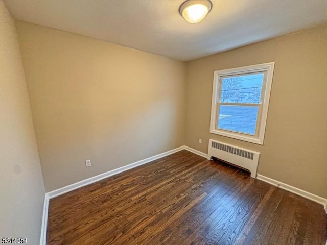 empty room with dark wood finished floors, radiator heating unit, and baseboards