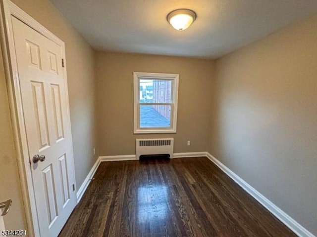 empty room with radiator, dark wood-style floors, and baseboards