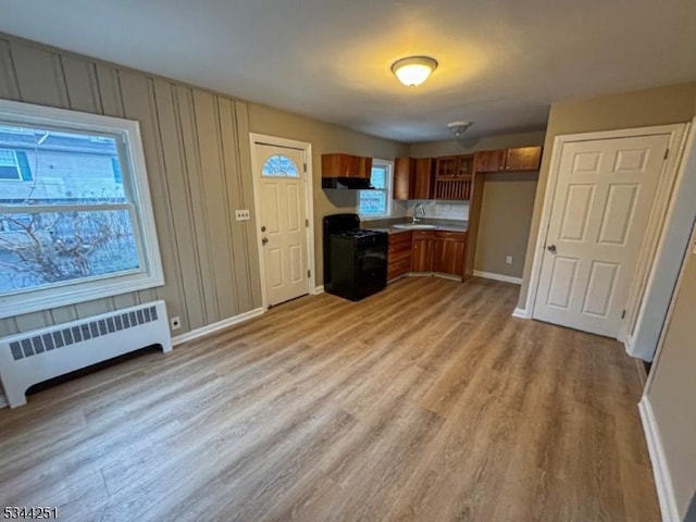 kitchen featuring brown cabinetry, gas range, light wood-type flooring, and radiator heating unit