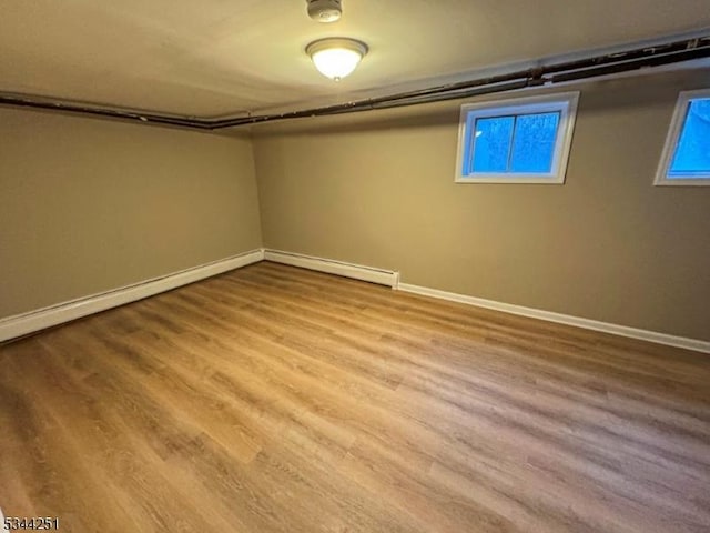 finished below grade area with a baseboard heating unit, baseboards, and wood finished floors