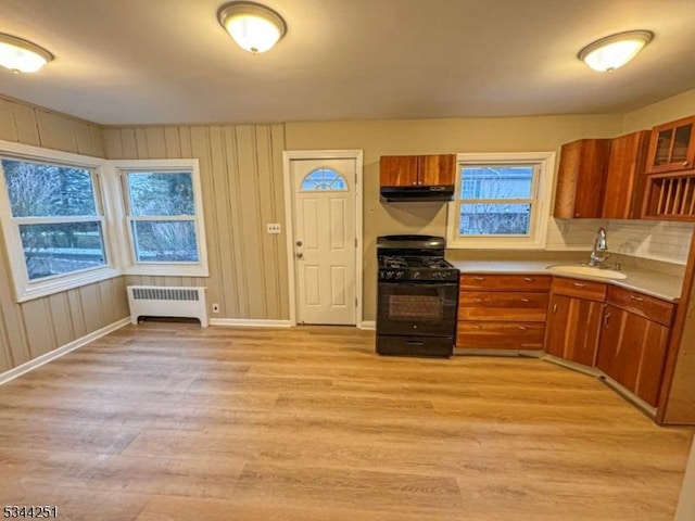 kitchen featuring gas stove, radiator, brown cabinetry, and a sink