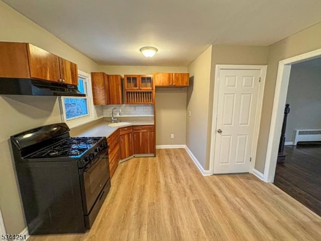 kitchen featuring brown cabinets, under cabinet range hood, a sink, black gas stove, and radiator