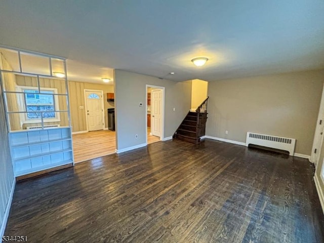 unfurnished living room with radiator, stairs, baseboards, and wood finished floors