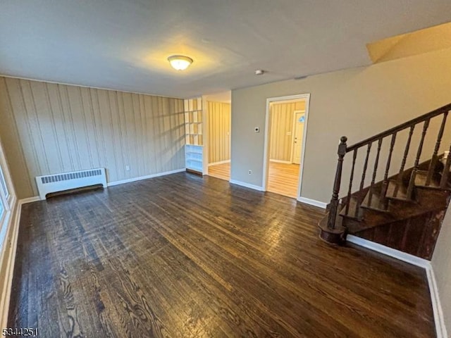 empty room with stairs, radiator heating unit, wood finished floors, and baseboards