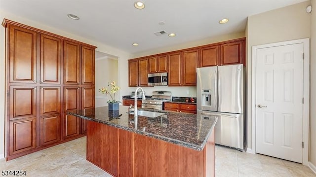 kitchen featuring dark stone counters, an island with sink, recessed lighting, a sink, and appliances with stainless steel finishes