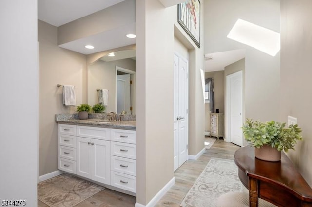 bathroom with baseboards, vanity, wood finished floors, and a skylight