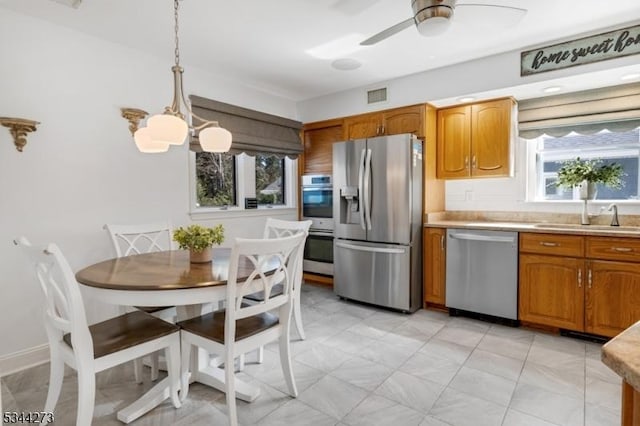 kitchen with light countertops, visible vents, brown cabinetry, stainless steel appliances, and a sink