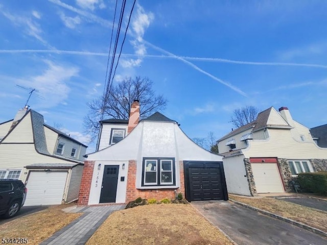 view of front facade featuring stucco siding, driveway, a chimney, and an attached garage