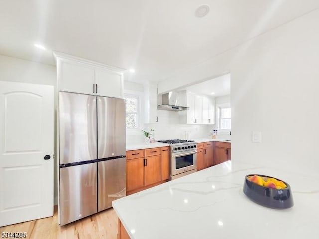 kitchen featuring light stone counters, white cabinetry, appliances with stainless steel finishes, and wall chimney range hood