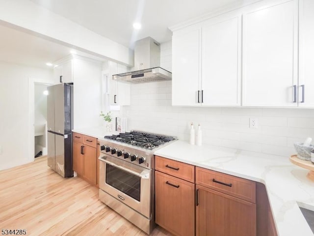 kitchen with backsplash, freestanding refrigerator, light wood-style floors, stainless steel stove, and wall chimney exhaust hood