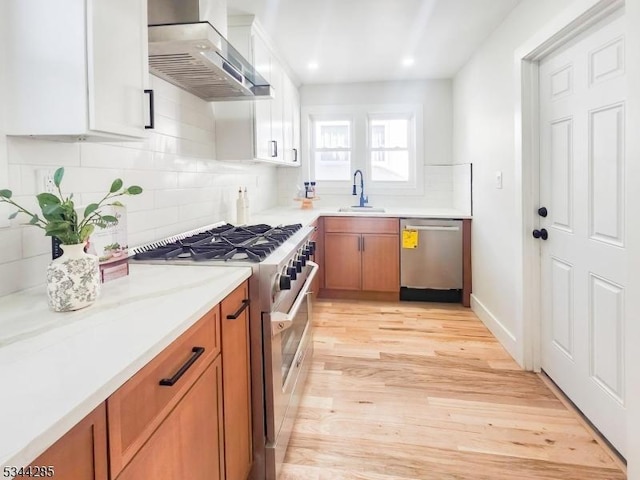 kitchen featuring brown cabinetry, stainless steel appliances, wall chimney range hood, and a sink