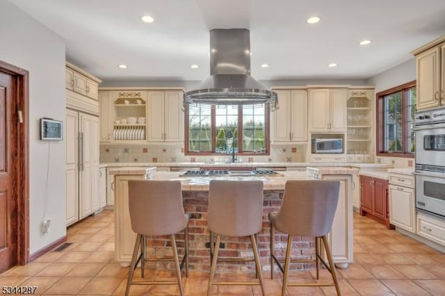 kitchen featuring cream cabinets, a kitchen bar, stainless steel appliances, and island range hood