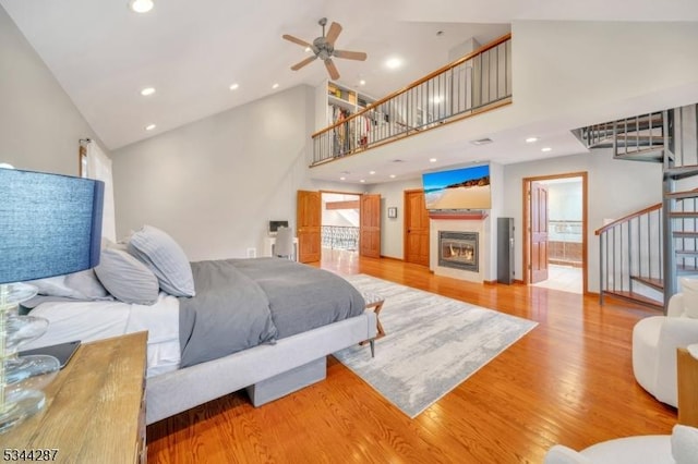 bedroom with light wood finished floors, recessed lighting, a warm lit fireplace, and high vaulted ceiling