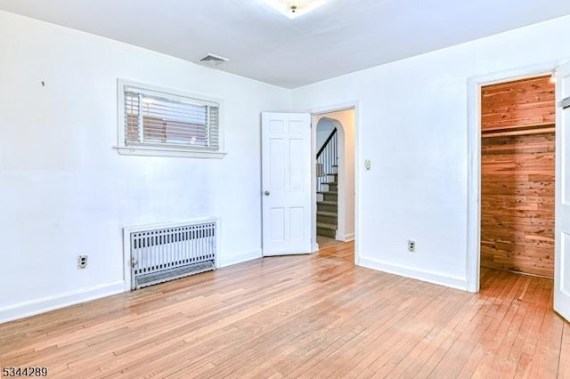 unfurnished bedroom with visible vents, light wood-style flooring, baseboards, and arched walkways