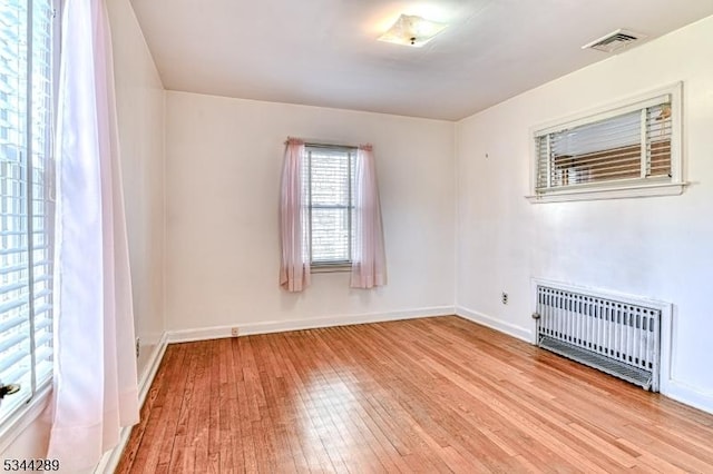 empty room featuring baseboards, radiator heating unit, light wood-style floors, and visible vents