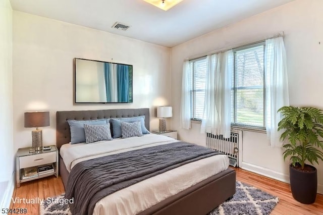 bedroom featuring baseboards, wood finished floors, visible vents, and radiator