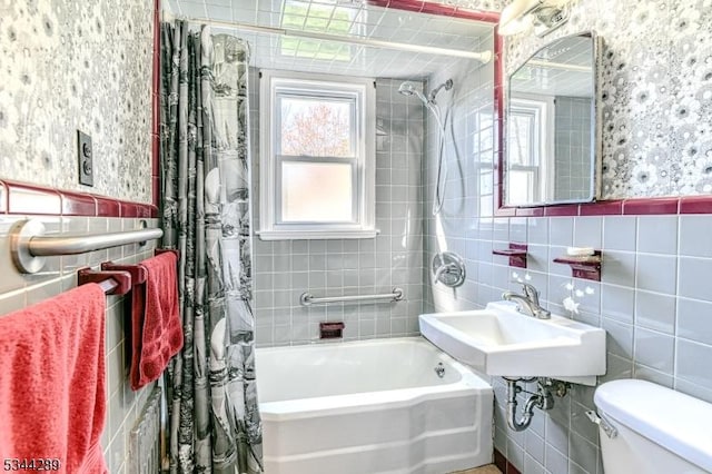 full bath with a sink, shower / bath combo with shower curtain, toilet, and tile walls