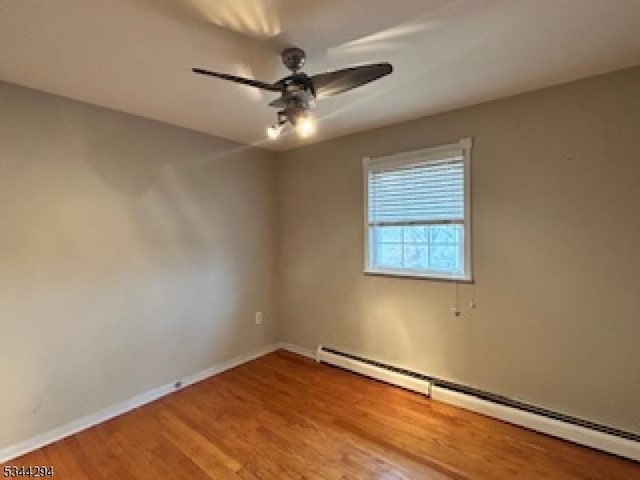 spare room featuring a baseboard heating unit, wood finished floors, a ceiling fan, and baseboards