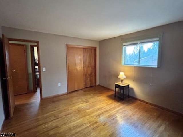 unfurnished bedroom featuring light wood finished floors, baseboards, and a closet