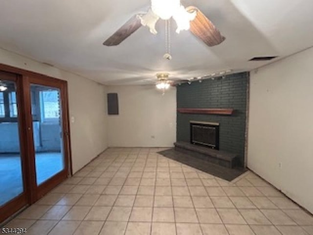 unfurnished living room with a brick fireplace, light tile patterned flooring, a ceiling fan, and visible vents