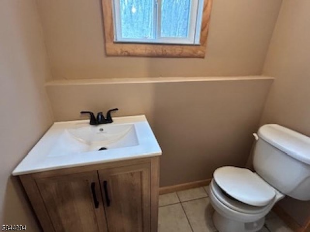 half bathroom with tile patterned floors, baseboards, toilet, and vanity