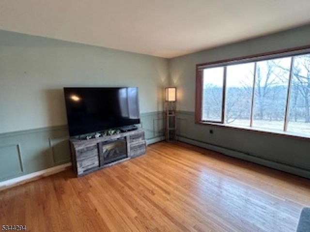 unfurnished living room featuring a fireplace, light wood-style floors, a wainscoted wall, and a baseboard heating unit