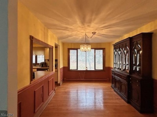 dining room featuring a baseboard heating unit, a chandelier, wainscoting, and light wood finished floors