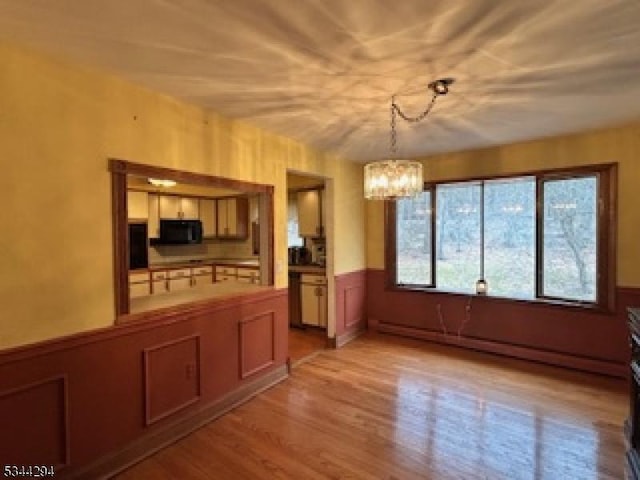 unfurnished dining area with a wainscoted wall, light wood-style flooring, and an inviting chandelier