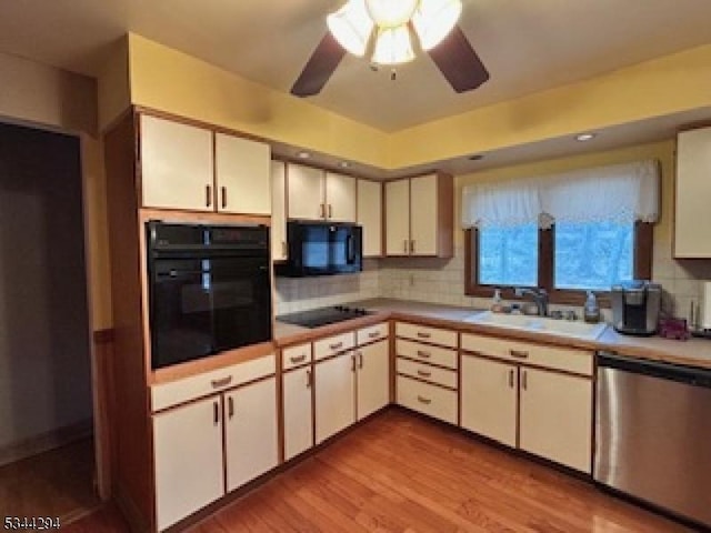 kitchen with backsplash, light wood-type flooring, light countertops, black appliances, and a sink