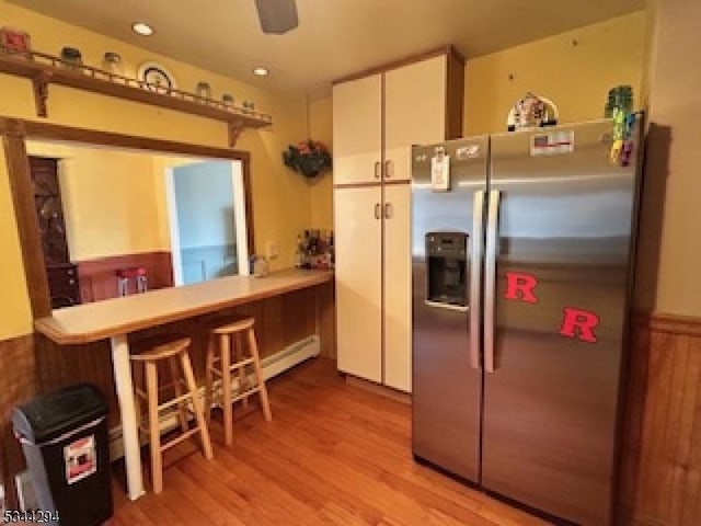 kitchen with a wainscoted wall, light countertops, light wood-style floors, stainless steel refrigerator with ice dispenser, and white cabinets