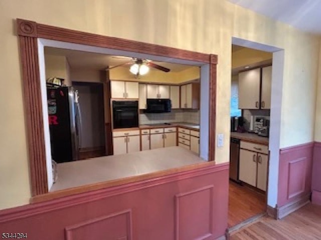 kitchen featuring a ceiling fan, light wood finished floors, a peninsula, black appliances, and tasteful backsplash