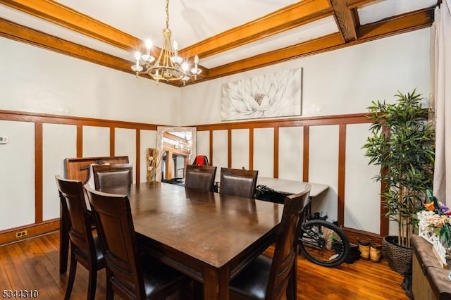 dining area with beam ceiling, a decorative wall, an inviting chandelier, and hardwood / wood-style flooring