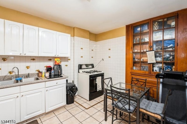 kitchen with range with gas stovetop, light tile patterned floors, white cabinetry, and a sink